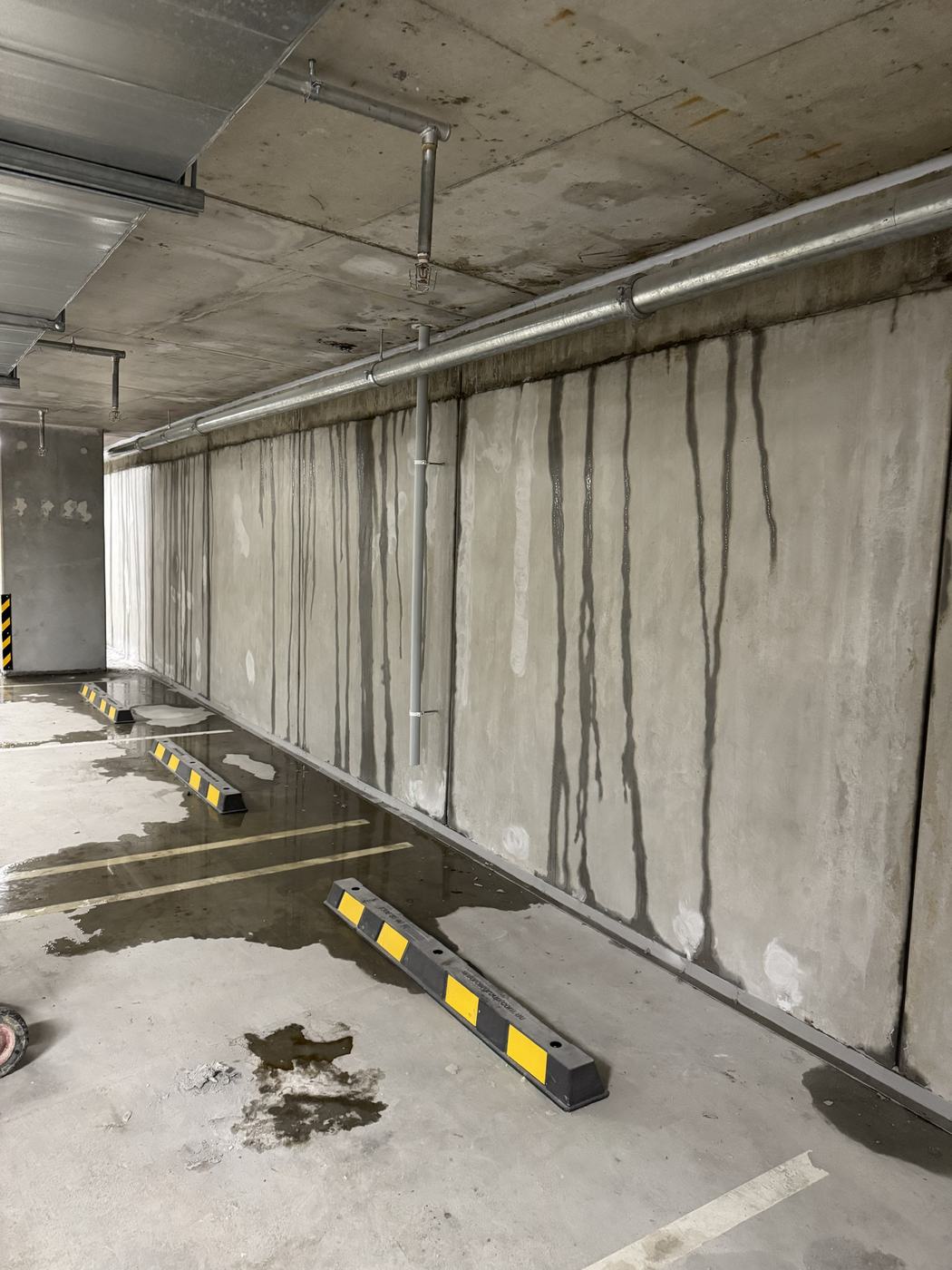 Water tracking down every panel joint along a basement carpark wall, with standing water across the floor